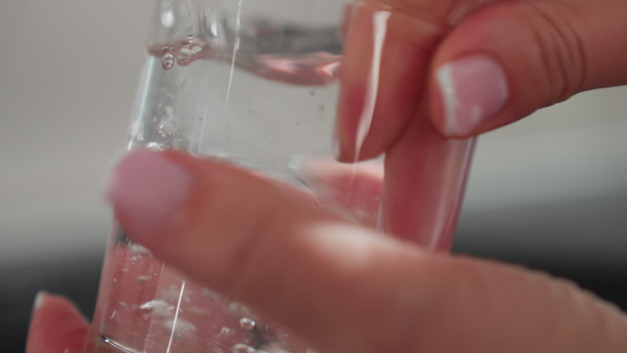 Close up of glass cup being thoroughly rinsed with neat water while person hand cleans inside rim with bubbles visible in water showing detailed focus on hygiene