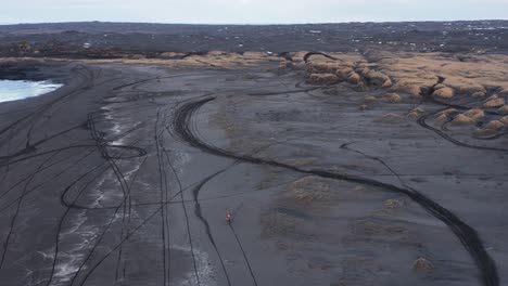 biker speeding on black sand beach of sandvik in iceland, aerial