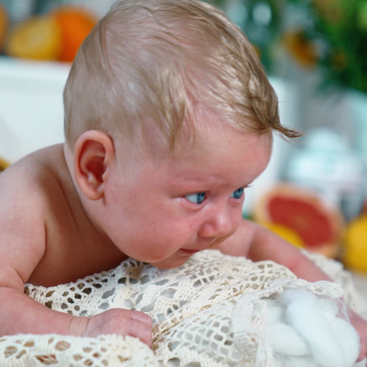 Beautiful blond Caucasian infant boy in yellow pants. Blue-eyed baby struggling to raise head. Close up. Blurred backdrop