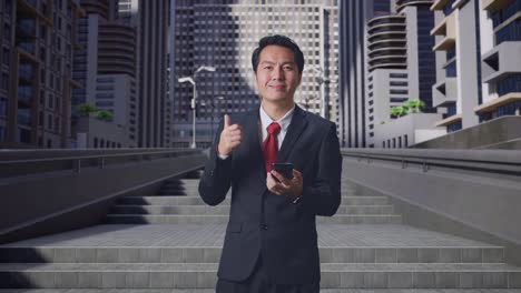 アジアのビジネスマンがスマートフォンを使い街に立っている間に親指を上げています