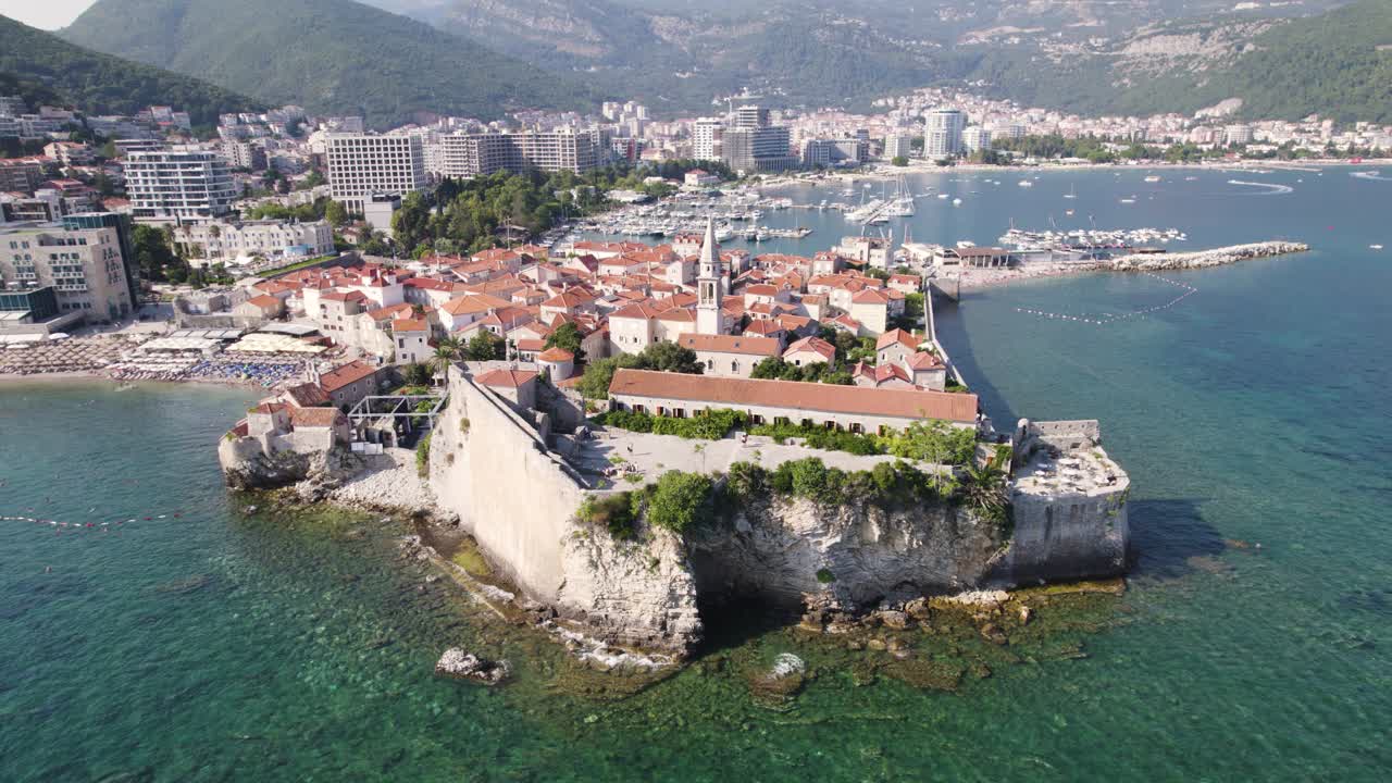 Aerial: Budva Citadel overlooking marina with city and mountain backdrop
