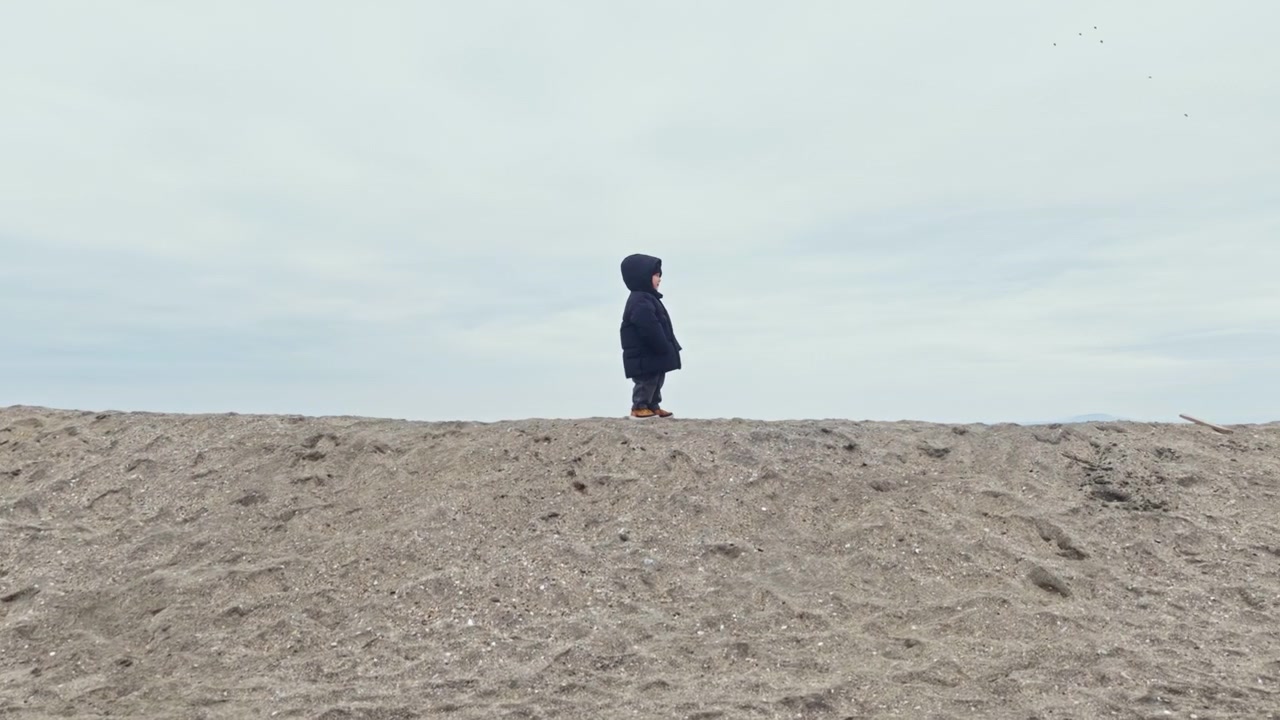 Un bambino cammina da solo su una collina sabbiosa sotto un cielo nuvoloso vicino alla spiaggia nel tardo pomeriggio.