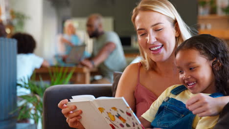 madre e hija leyendo un libro en casa junto con una familia de varias generaciones en el fondo
