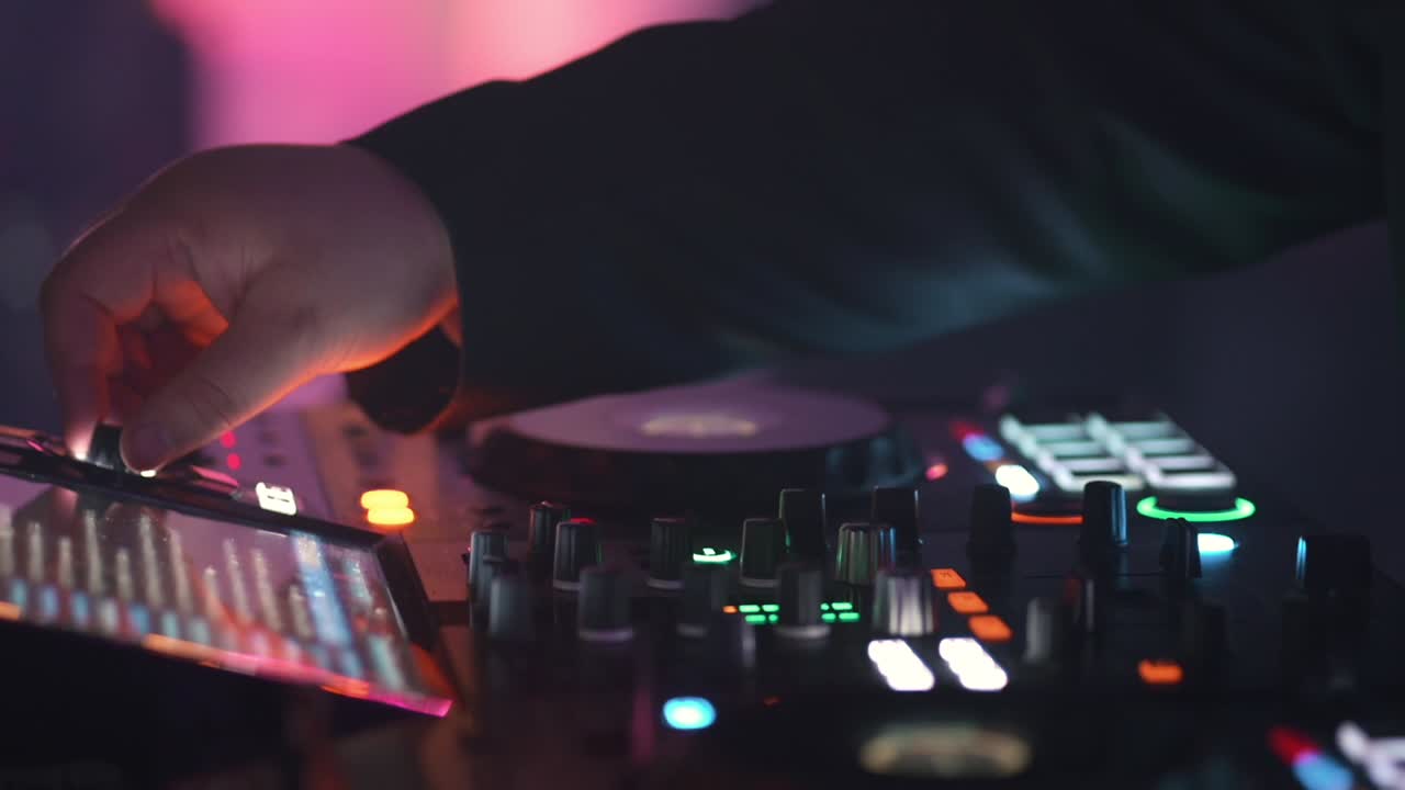 Primo piano delle mani di un DJ che mixa musica sul fader di un controller durante una festa elettronica con luci da discoteca.