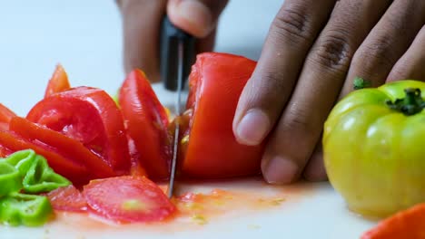 chef cortando un tomate rojo en una superficie blanca, derramando jugo y pepitas