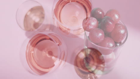 compuesto de vasos de vino de rosas sobre uvas rojas sobre un fondo rosa