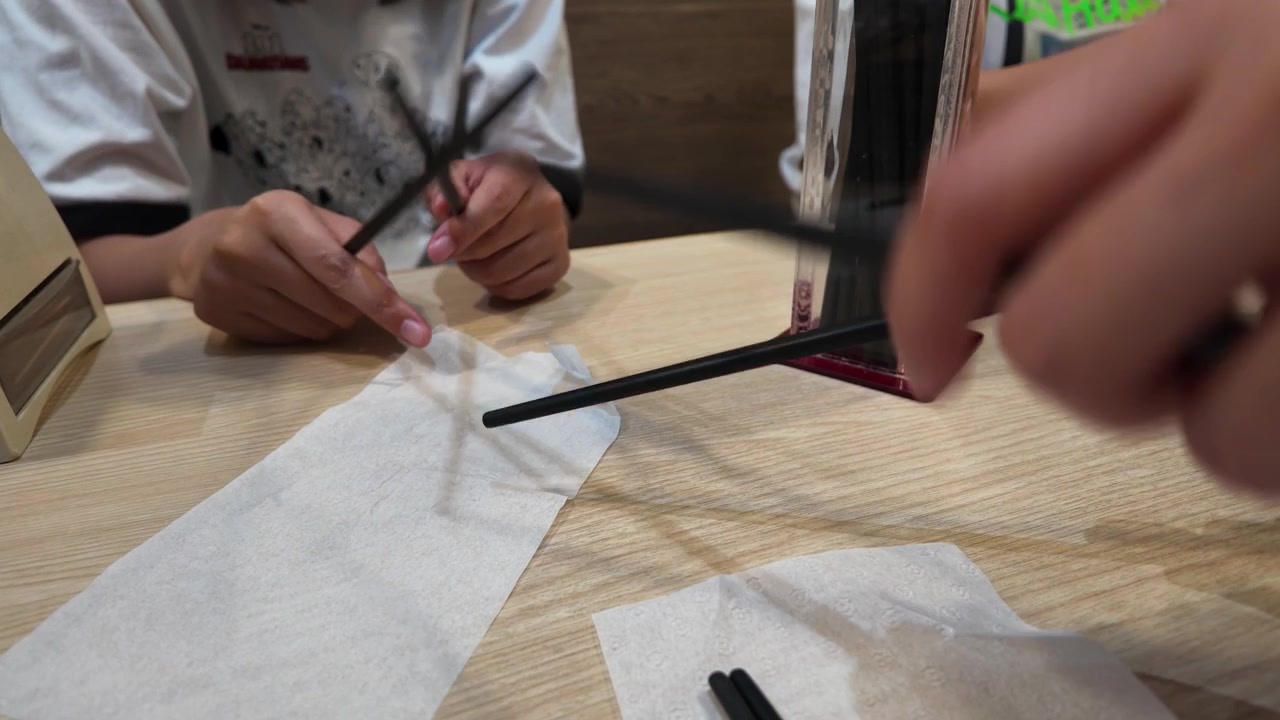 Close-up shot of people handling chopsticks over a wooden table in Bangkok, Thailand.