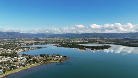 aerial of lake illawarra estuary and suburbs under clear blue sky in new south wales, australia, panoramic establishing for real estate