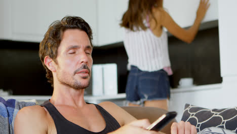 hombre viendo la televisión mientras la mujer trabaja en la cocina 4k