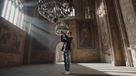 young man photographing a grand chandelier in a historic hall