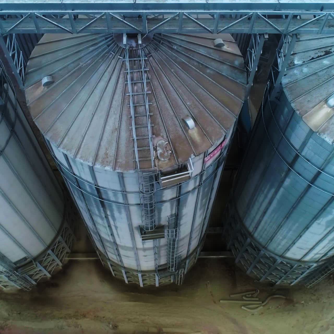 Huge mighty cisterns for grain storage at elevator plant. View on the metal tanks connected with each other by a support. Aerial perspective