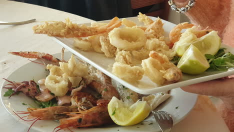 manos de mujer sirviendo anillos de calamar en un plato de mariscos, de cerca
