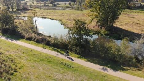 motociclista solitario montando a través de un paisaje con campos de hierba y árboles a lo largo de la carretera con un río serpenteante además