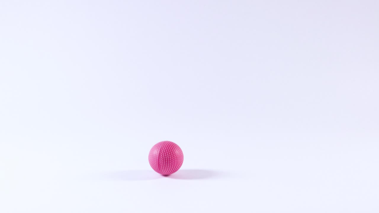 A pink ball bounces on a white surface