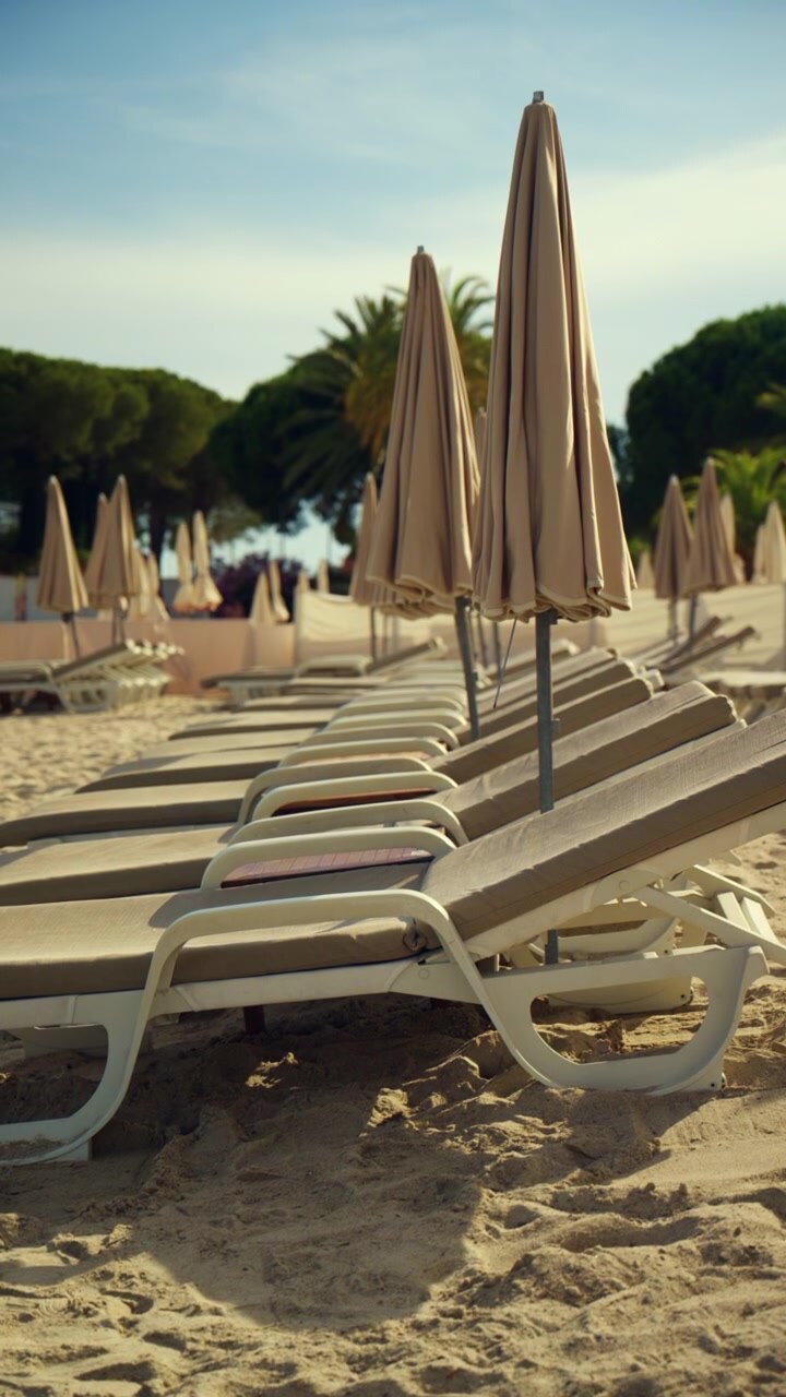 Fila di lettini da spiaggia non occupati e ombrelloni piegati su una spiaggia sabbiosa sotto un cielo azzurro e limpido, che evoca svago e vacanze estive