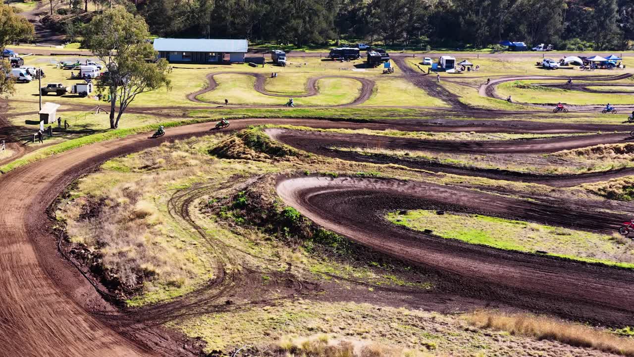 Motorbike rider navigates winding dirt track in bright daylight at rural motocross facility