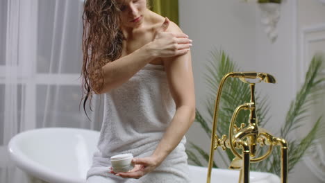 beauty and body care female elbow pain and health care concept. slow motion of caucasian woman applying lotion cream moisturizer relaxing in bed in white cozy apartment near window. hand touching careful