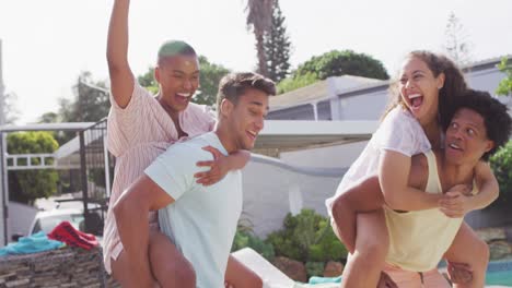 Two-happy-diverse-male-friends-holding-piggyback-female-friends-in-backyard-at-pool-party