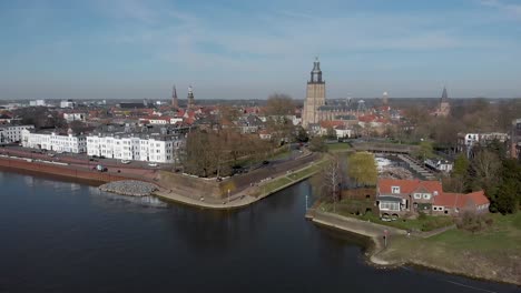 picturesque aerial rotate showing medieval hanseatic city zutphen, the netherlands, with entrance to small vispoorthaven or gelre port and cargo ship passing on river ijssel against a blue sky