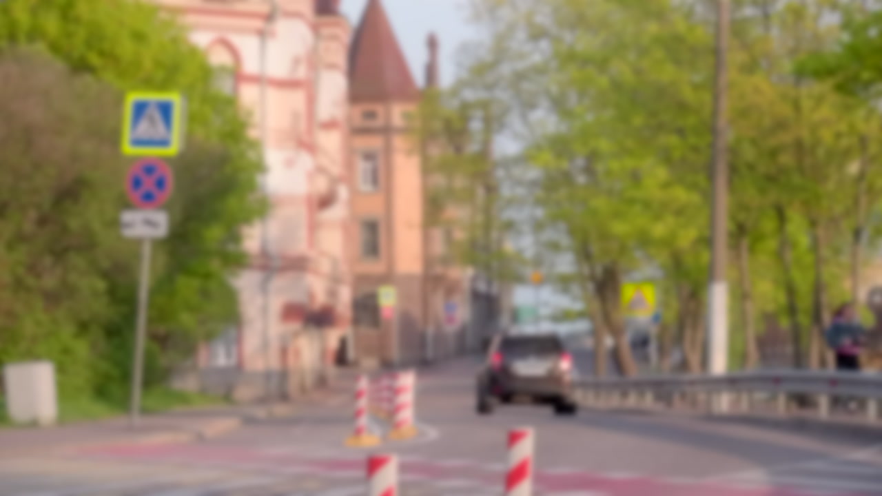 City Street Black Suv Bollards Near Crosswalk, Blurred Traffic Passing Historic Building Facade, Spring Trees. Creative