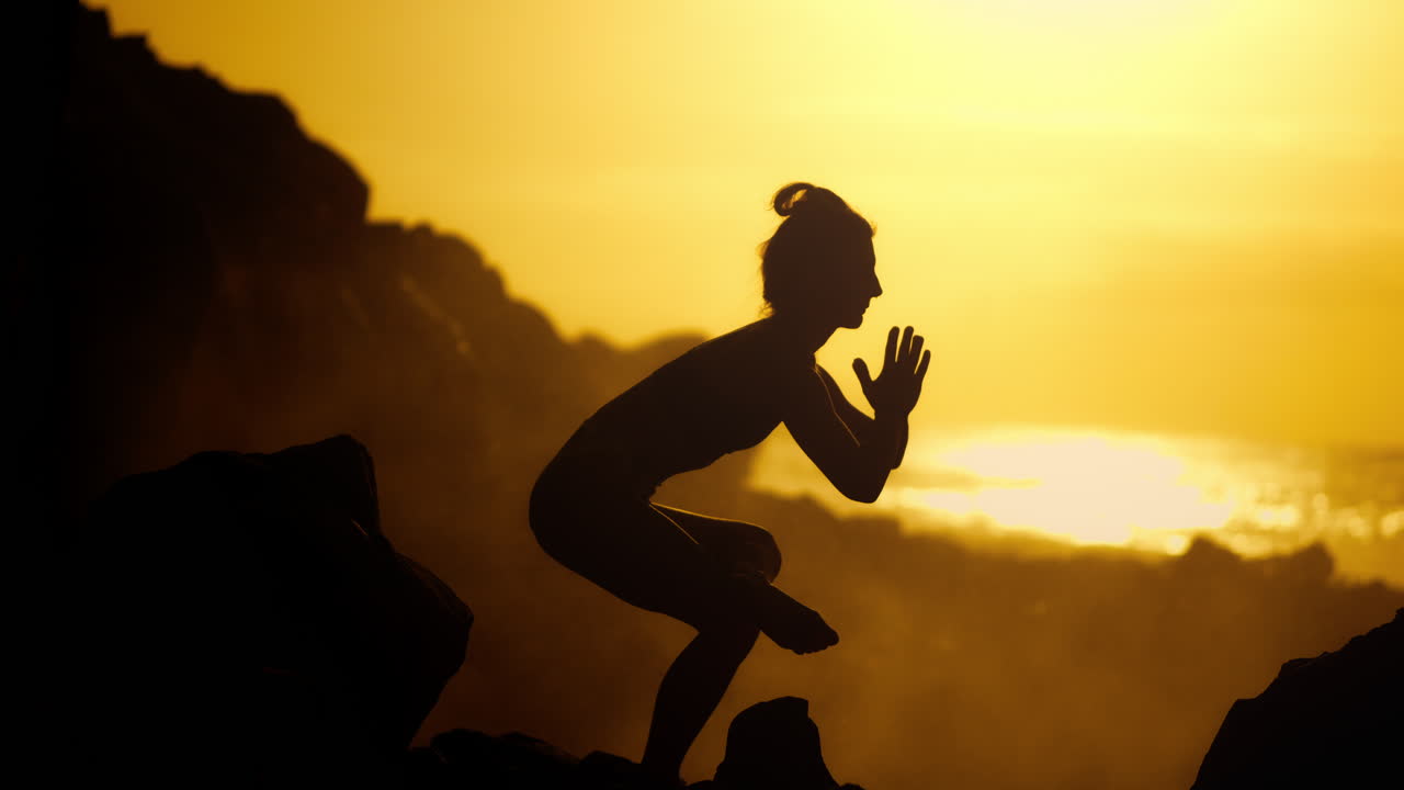 Woman practicing yoga at sunset on a rocky beach