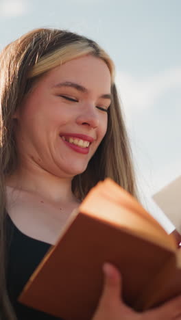 primer plano de una joven pensativa vestida de negro hojeando un libro al aire libre bajo un cielo brillante, encontrando un papel escondido dentro de las páginas y sonriendo emocionada, mientras la luz del sol ilumina suavemente su rostro