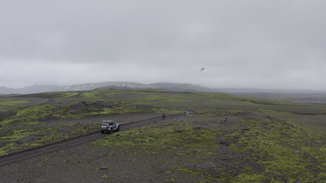 안개 낀 날 아이슬란드의 고지대 도로를 달리는 자동차 뒤를 잇는 자전거 - 공중 드론