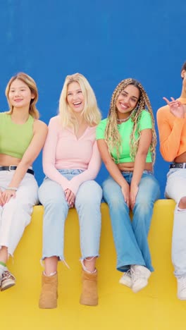 Multi ethnic women sitting on a colorful urban wall waving