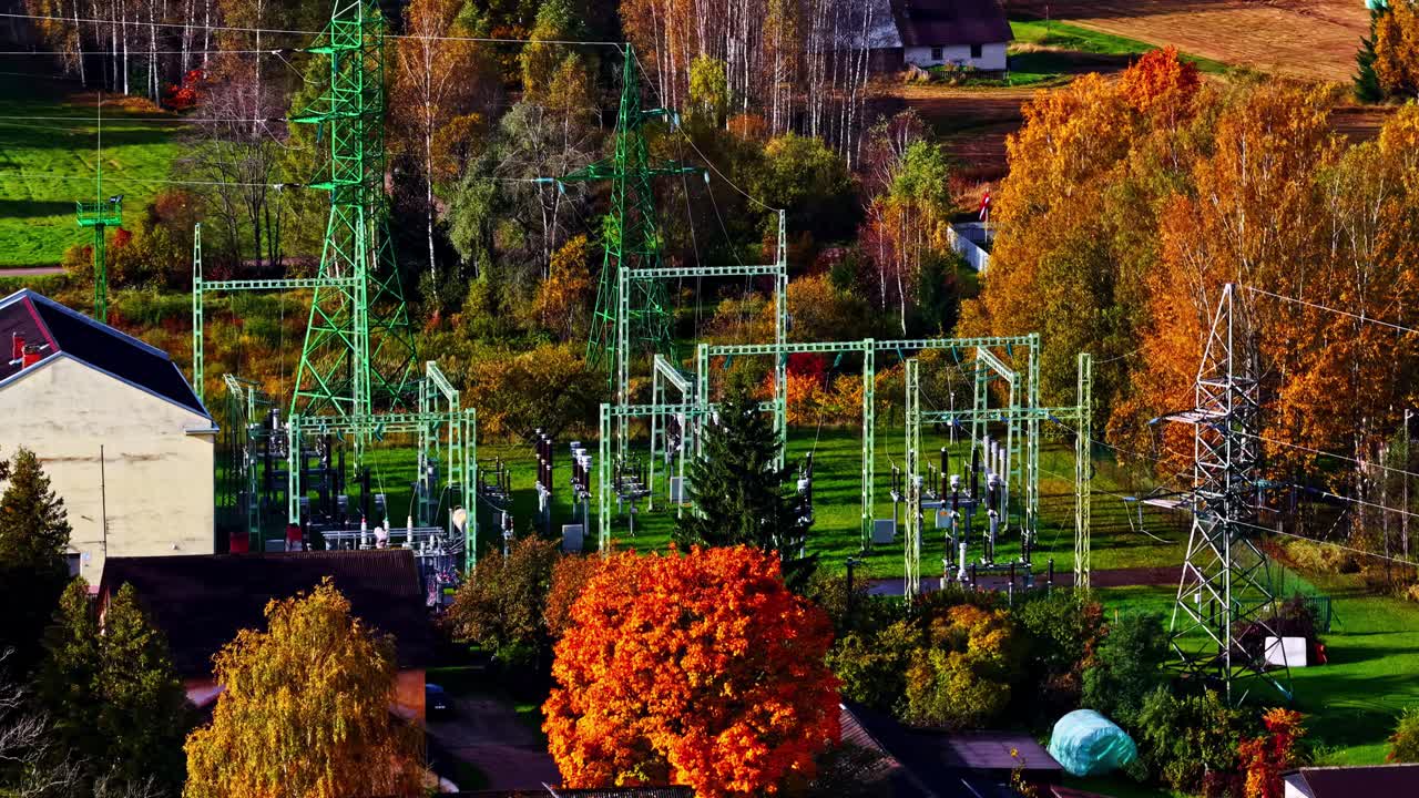 Electric transformer supply power station through autumn trees with red and orange leaves in soft light, aerial