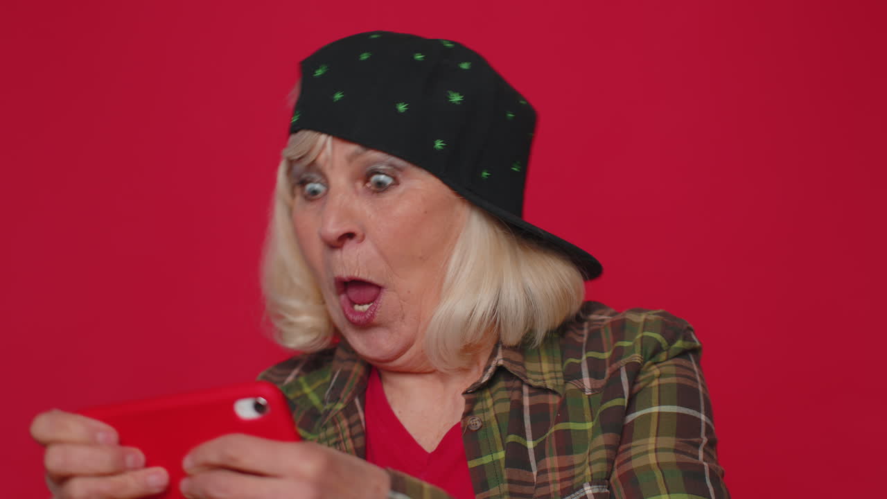 걱정스럽고 재미있고 중독된 노인 여성이 드폰에서 드라이브 레이싱 비디오 게임을 열정적으로 연주합니다.