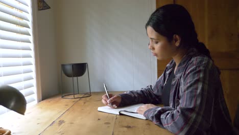 Young-Puerto-Rican-female-writing-inspirational-feelings-in-personal-journal-at-rustic-table