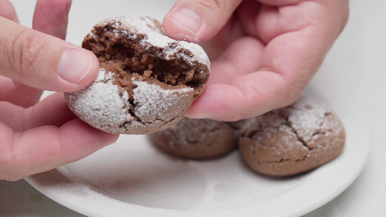 Slow motion close-up of hands breaking a sugar-dusted chocolate cookie