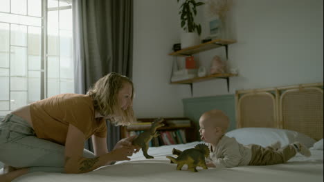 mother and baby playing with dinosaurs on bed