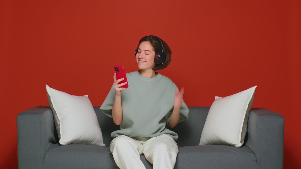 소녀는 스마트폰을 통해 무선 헤드폰으로 멋진 음악을 듣습니다. 긍정적 인 분위기. 전화에 대한 음악 앱. 빨간색 배경에 고립되어 있습니다.