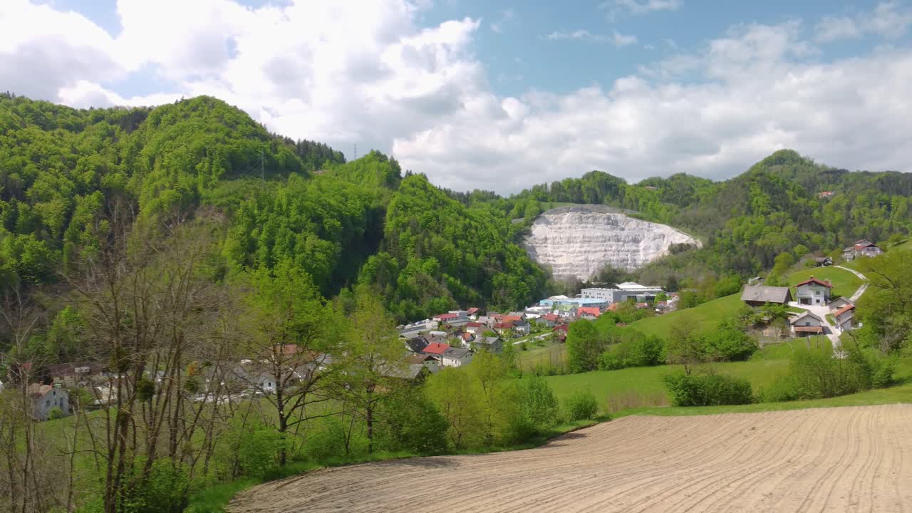campo arado junto a un pequeño asentamiento con cantera de piedra en segundo plano.