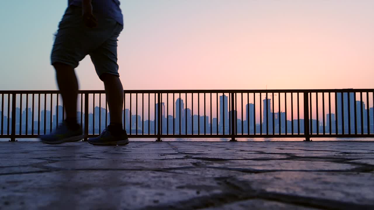 cámara lenta, silueta: un hombre haciendo ejercicio-caminando con un horizonte de la ciudad en el fondo durante el amanecer en sharjah, emiratos árabes unidos