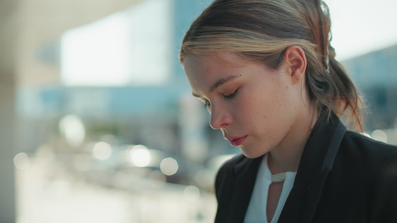 Primo piano di una donna d'affari che scrive al telefono con espressione seria all'aperto, effetto bokeh sullo sfondo che mette in risalto l'ambiente urbano, vestita con abbigliamento professionale