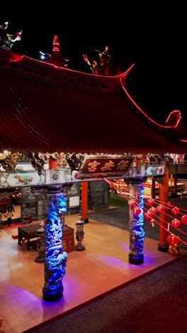 vertical drone footage captures a serene buddhist temple entrance illuminated by beautiful warm lights with intricate carvings and traditional lanterns creating a peaceful and spiritual atmosphere