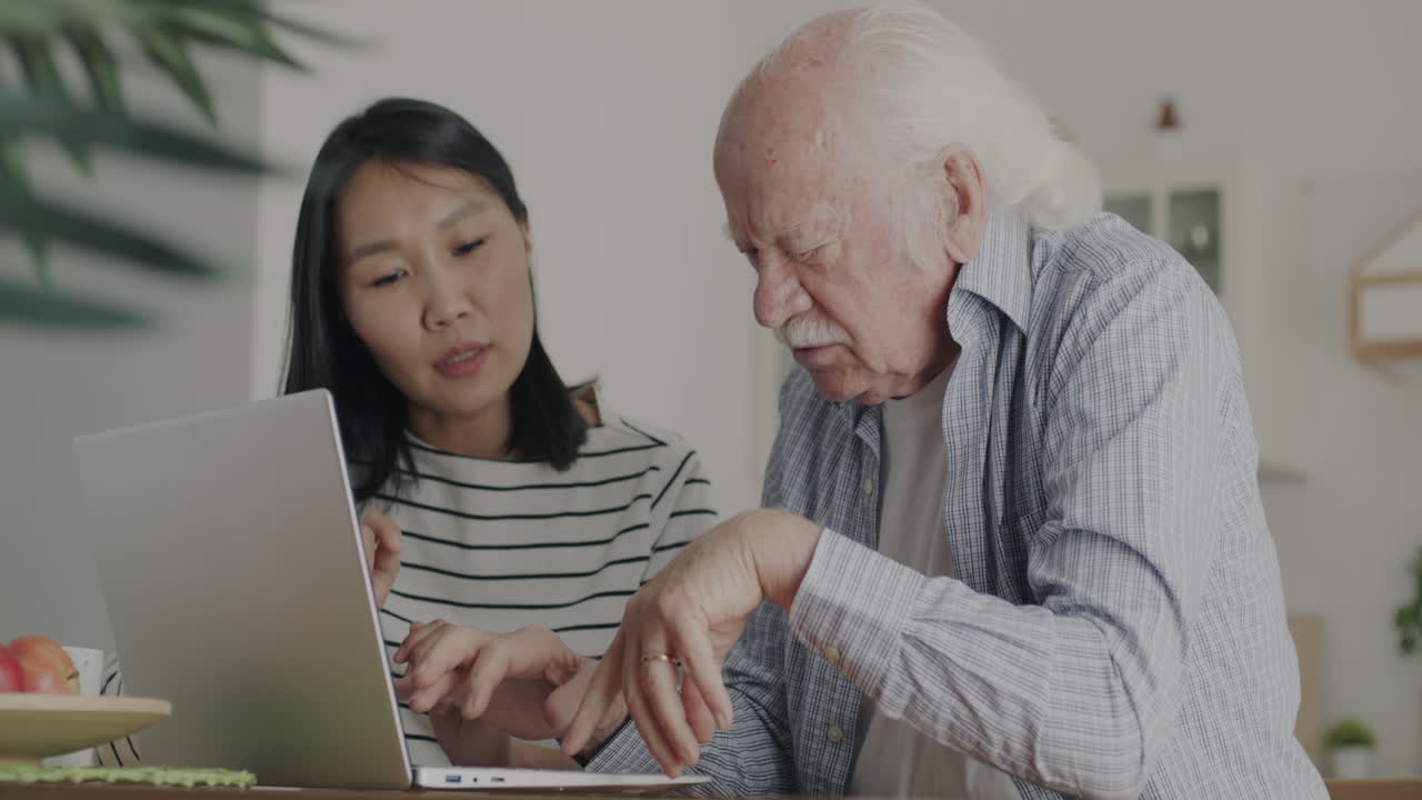 Young Woman Helping Elderly Man with Laptop