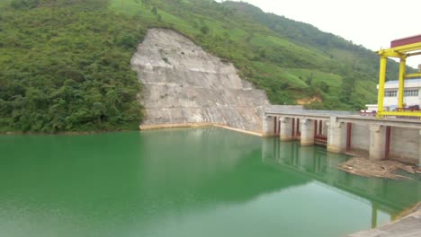 a hydro electric dam sits in a valley creating a bluish green lake in the mountains of northern vietnam