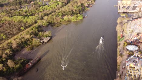 a dynamic aerial footage of a cruising passenger boats along the riverside of parque de la costa amusement park at the tigre area in buenos aires