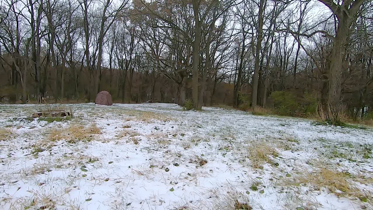 POV from the rear of off road vehicle ATV while driving on a snow covered trail through the woods on an cloudy winter afternoon; the trail goes past a portable deer stand; point of view