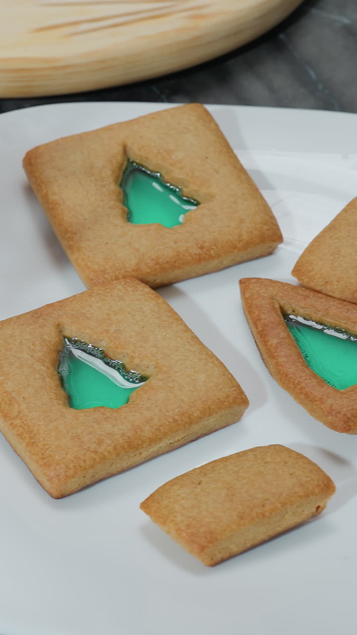 Primo piano di un fiore decorativo con biscotti su un piatto bianco, ripieno verde visibile all'interno, vassoio di legno con altri biscotti sullo sfondo, che mostra biscotti decorati fatti in casa con un fascino festoso