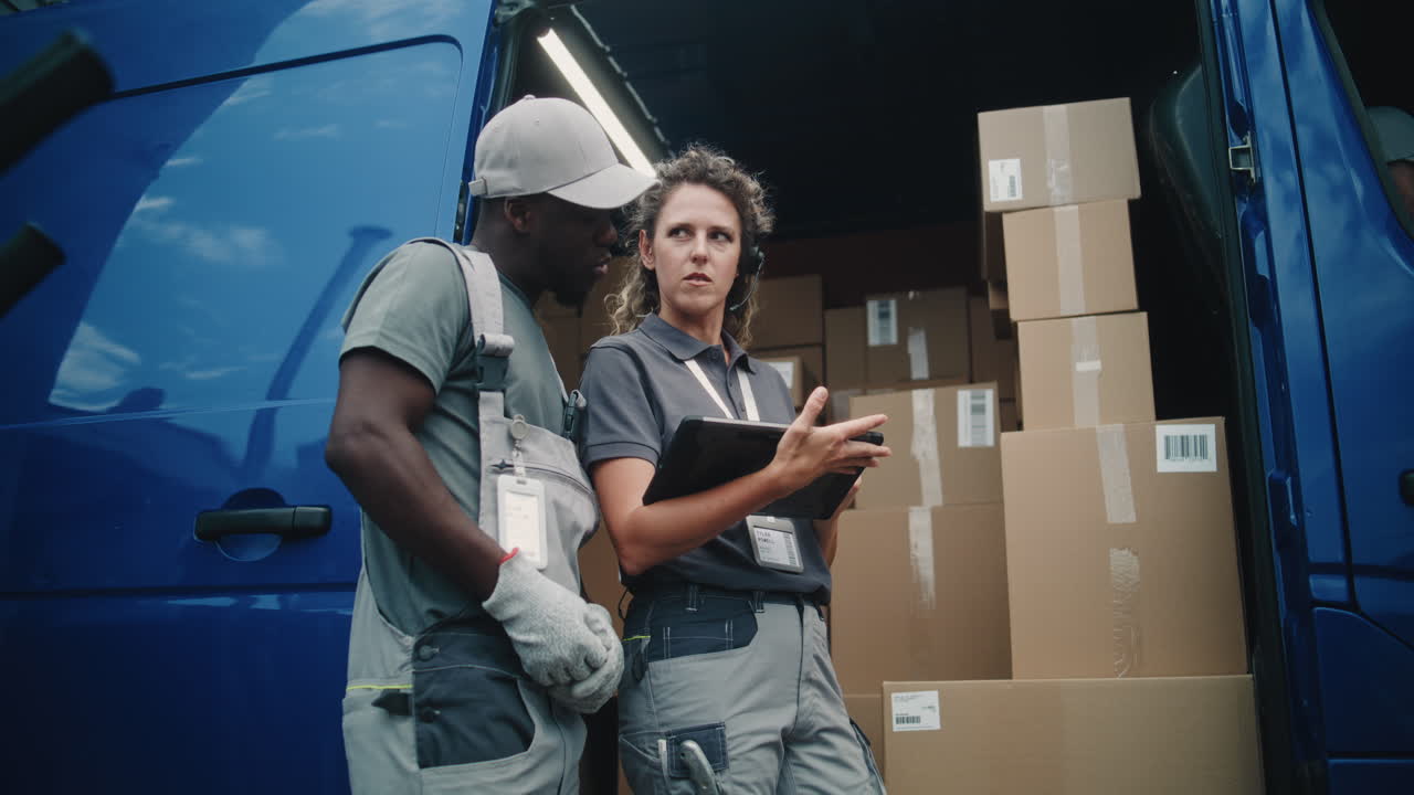 Two diverse delivery workers checking packages on a tablet next to a cargo van filled with boxes