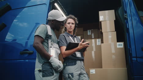 two diverse delivery workers checking packages on a tablet next to a cargo van filled with boxes