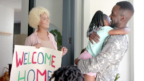 african american soldier father in hugs daughter; biracial mother holds welcome home sign