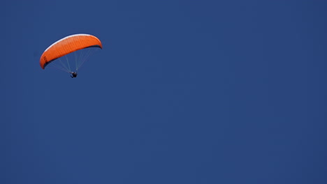 un paracaídas naranja flota en un cielo azul en medio del día, sobre los alpes suizos, obwalden