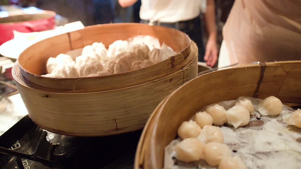 Close-up shot of various dim sum and white steamed buns inside traditional bamboo steamer baskets