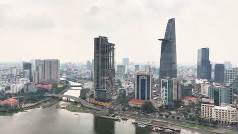 Downtown Ho Chi Minh City skyline with the Bitexco Financial Tower, Saigon River, modern skyscrapers, bridges, and a prominent unfinished high-rise under cloudy skies in Vietnam’s financial hub