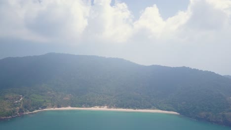 Aerial-tracking-shot-above-ocean-toward-lush-island-with-beach-on-cloudy-day-in-Thailand